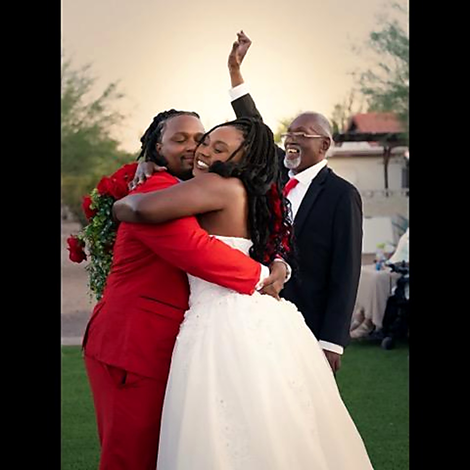 Bride in a beaded white ballgown embracing her groom in a red tuxedo after their outdoor Arizona wedding ceremony - Strictly Weddings Phoenix AZ